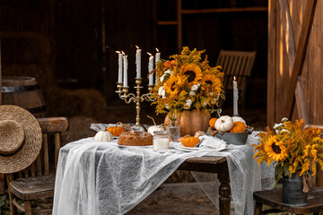 Cozy autumn table decoration for a thanksgiving party outdoors. Centrepiece with sunflowers, candles, pumpkins as decor. Elegant wedding fall arrangement, beautiful setting for a romantic lunch.