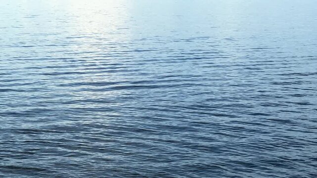 Blue rippling water surface on a sunny day with light reflection across the calm ocean or lake, serene fluid background footage