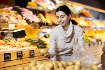 Young woman buyer choosing fresh potatoes in vegetable shop