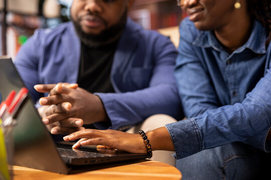 Casual man and woman opening laptop on the coffee table to solve daily tasks, doing remote freelance work online. Black couple surfing the web and multitasking in their loft apartment. Close up. - Powered by Adobe