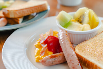 Western breakfast with toast, scrambled eggs, sausages, fruit and coffee
