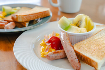 Western breakfast with toast, scrambled eggs, sausages, fruit and coffee
