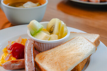 Western breakfast with toast, scrambled eggs, sausages, fruit and coffee
