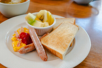 Western breakfast with toast, scrambled eggs, sausages, fruit and coffee
