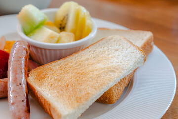 Western breakfast with toast, scrambled eggs, sausages, fruit and coffee
