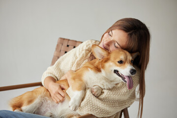 Woman hugging corgi on a cozy chair at home showing human pet bond