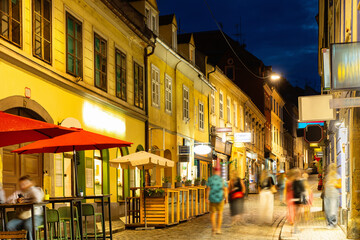 Naklejka premium Warm summer evening on Tkalciceva Street in Zagreb, Croatia, with glowing lights, buzzing cafes, and people enjoying lively nightlife on cobblestone road