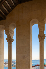 Fototapeta premium View from bell tower of Saint Domnius Cathedral in Split, Croatia, through stone arches with carved capitals, overlooking coastal cityscape with tiled rooftops and Adriatic sea glowing at sunset