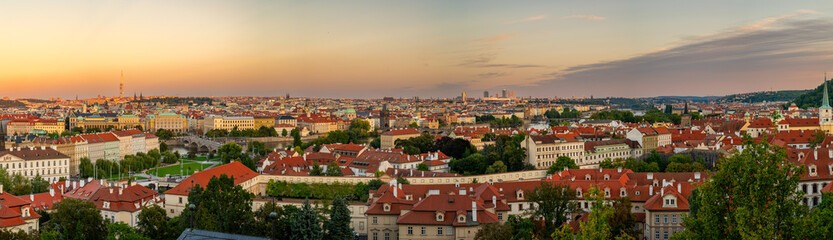 A breathtaking panoramic view of Prague showcasing the historic cityscape with red rooftops, the majestic Prague Castle, and the winding Vltava River under a golden sunset sky.