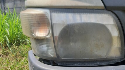 Front car light lens with dull texture and faint yellow discoloration from age and weather. © robbitommi