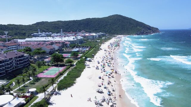 Aerial view of a paradisiacal beach with many people on the sand and in the sea, Brava Beach in Florian&oacute;polis Santa Catarina blue sea with vibrant summer colors, beach with many tourists.