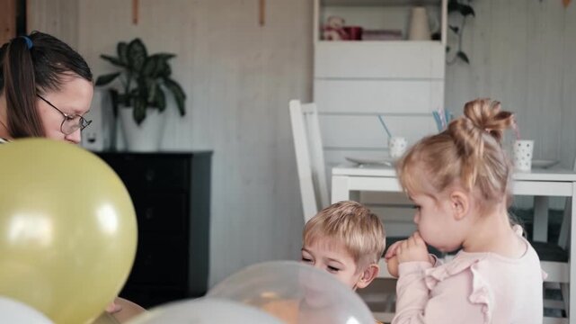 Family Fun Children Joyfully Blowing Up Balloons. Kids inflating balloons, prepare for birthday party. 3,6, 14 years old siblings racing blowing balloon, decorate the room. Bonding time together. Joy