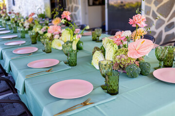 Elegant Dining Table Set Up with Pink Plates, Green Glassware, and Colorful Floral Arrangements for a Luxurious Gathering Experience