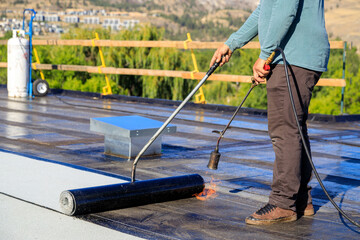 Roofer applying torch to bitumen membrane on torch down roof