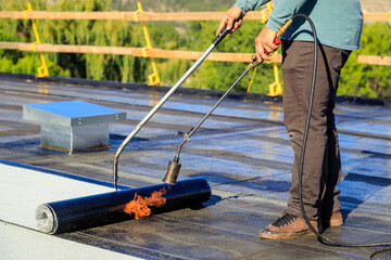 Roofer applying torch to bitumen membrane on torch down roof