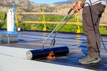 Roofer applying torch to bitumen membrane on torch down roof