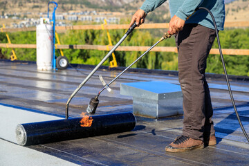 Roofer applying torch to bitumen membrane on torch down roof