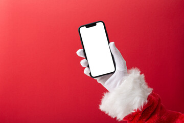 Christmas concept, Santa Claus hand holding a smartphone with blank screen with copy space on red background