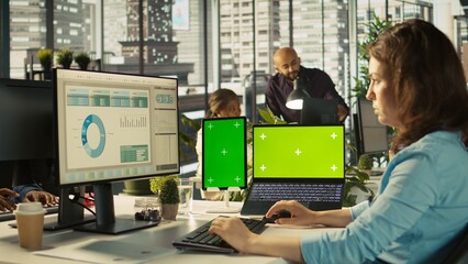 Office clerk uses chroma key devices to read data statistics on display after audit. Employee at work using green screen laptop and tablet to check progress done on commissioned project, camera B