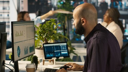 Accountant in busy workplace talking with colleagues while inputting financial figures on PC. Employee working in modern office chatting with coworkers while crosschecking data, camera A