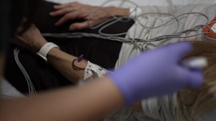 Mature woman in emergency hospital room is connected to heart and EKG monitors while receiving care. Medical staff attend to her needs for health evaluation.
