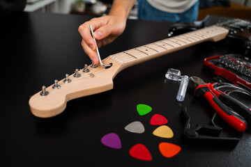 Guitar Adjustment with Hex Key. Guitarist uses a hex key to adjust bridge saddles and string height. Guitar strings are adjusted with a hex key at the bridge for accurate intonation and comfort.
