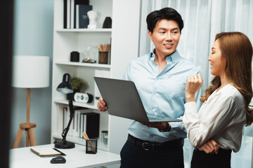 Obraz premium Smiling Asian coworkers standing while talking planning marketing report project on laptop casual day at modern office. Analyzing successful customer need in new social media online channel. Infobahn.