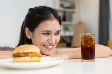 Smiling women looking at burger and soda on table with excitement and anticipation. Concept of fast food craving, guilty pleasure, or enjoying favorite comfort food.