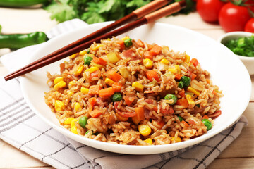 Tasty fried rice and chopsticks on light wooden table, closeup