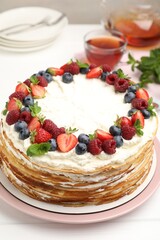 Delicious crepe cake with fresh berries and tea on white wooden table, closeup