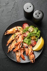 Tasty grilled shrimps served with salad and lemon on black table, flat lay. Delicious seafood dish