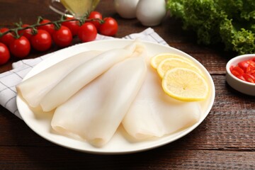 Pieces of raw squids with lemon on wooden table, closeup