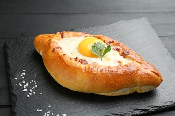 Tasty khachapuri with cheese, egg, salt and parsley on black table, closeup