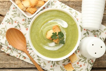 Tasty broccoli cream soup with croutons served on wooden table, flat lay
