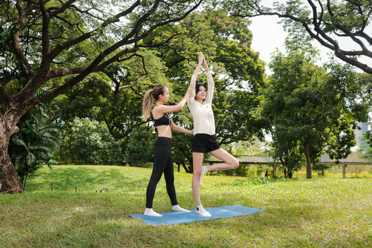 Asian woman in sportswear stretching workout outdoor on yoga mat in park with her trainer. Sporty buddy women work out together in green garden. Sporty girl engage in exercise with partner in nature.