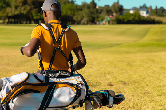 African American golfer checking wristwatch on golf course with golf bag and sunglasses, copy space