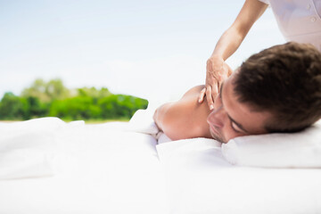 Male client lying on massage table in white linens therapist pressing shoulder blade on spa terrace