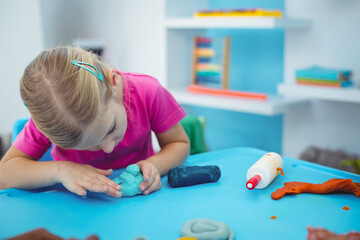 Modeling clay pieces resting on bright blue plastic table with glue bottle and colorful shelving