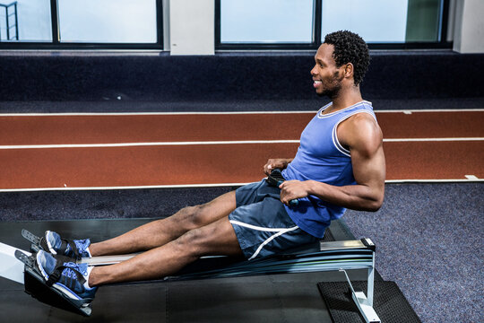 African American man pulling handle on rowing machine in gym wearing sports shoes near track lanes