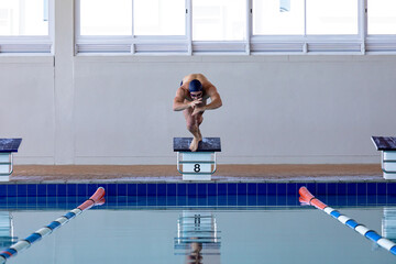 Male swimmer crouching on starting block number eight above turquoise tiled pool lanes