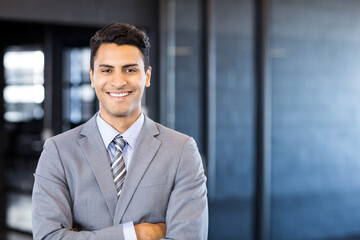 Executive smiling and crossing arms in grey suit and striped tie in modern office corridor