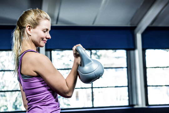 Fototapeta Adult female performing gray kettlebell curl near blue-shaded windows in gym under steel beams