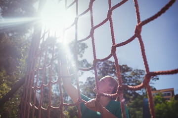 Woman climbing rope net outdoors wearing green athletic shirt and fingerless gloves, copy space