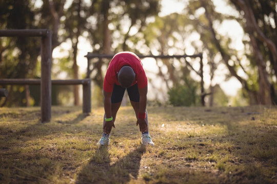 Fototapeta lone man bending and stretching legs wearing fitness tracker near wooden bars in grassy park