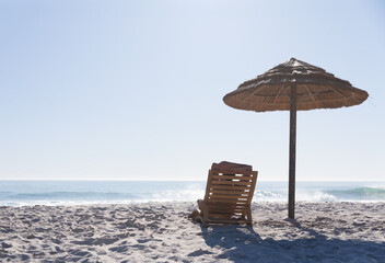 Naklejka premium Wooden lounge chair draped red towel standing under straw parasol on beach facing sea, copy space