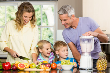 Family of four slicing fruits on cutting board and operating blender on kitchen countertop