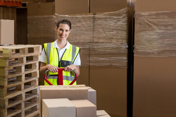 Red manual pallet jack waiting in warehouse, among stacked cardboard boxes and wooden pallets