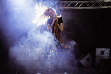 Female singer performing gripping microphone stand draped scarf on concert stage with smoke effects