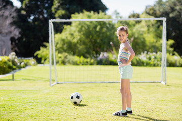 Obraz premium Female child standing on backyard lawn in front of goalpost smiling at soccer ball, copy space