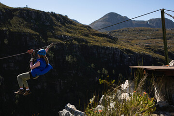 Female tourist zip-lining across mountain canyon on steel cable with red pulley, copy space